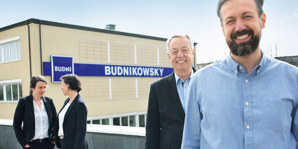 Die Unternehmerfamilie Budnikowska steht auf einem Flachdach in Hamburg um Hintergrund ist das Firmenlogo zu sehen.