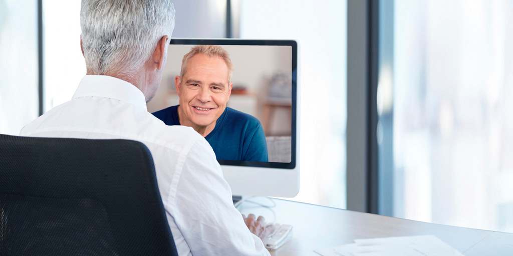 Arzt sitzt am Schreibtisch und spricht per Webcam mit seinem Patienten
