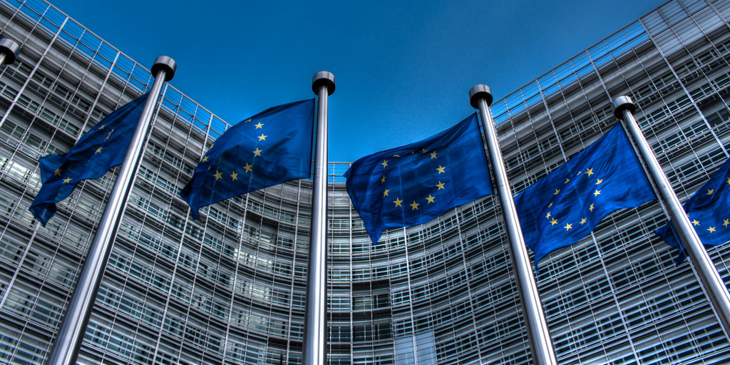 EU-Flaggen wehen vor dem Gebäude der EU-Kommission in Brüssel, unter einem strahlend blauen Himmel.