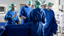 Ein Team aus zwei Ärzten und zwei OP-Schwestern führt eine Operation durch. Eine OP-Schwester reicht ihrer Kollegin ein OP-Besteck.