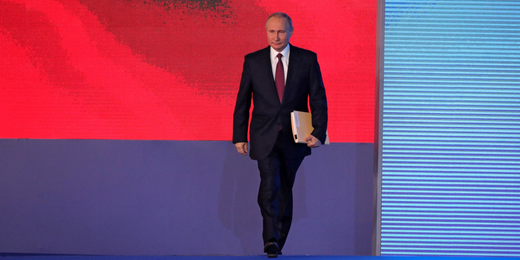 Vladimir Putin enters the stage for his Presidential Address to the Federal Assembly. In the background of the stage, one can see a projection of the Russian flag.