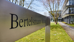 Aufnahme des Schildes mit der Aufschrift "Bertelsmann Stiftung" am Haupteingang zum Stiftungsgebäude, der Haupteingang ist im Hintergrund zu sehen