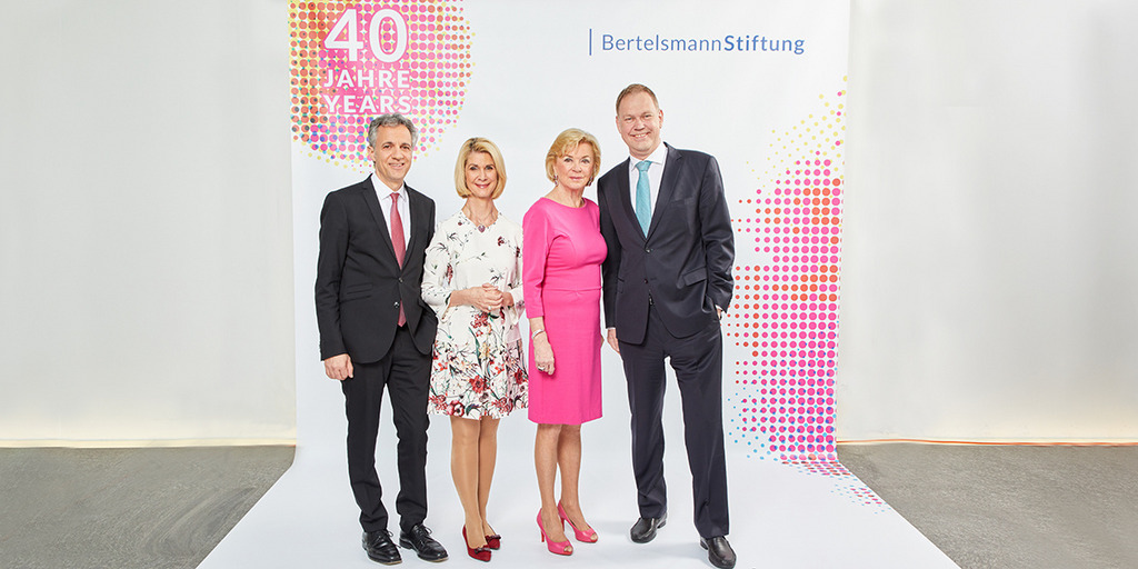 Group picture of the four members of the Bertelsmann Stiftung's Executive Board in front of a poster bearing the inscription "40 years of the Bertelsmann Stiftung" in German.