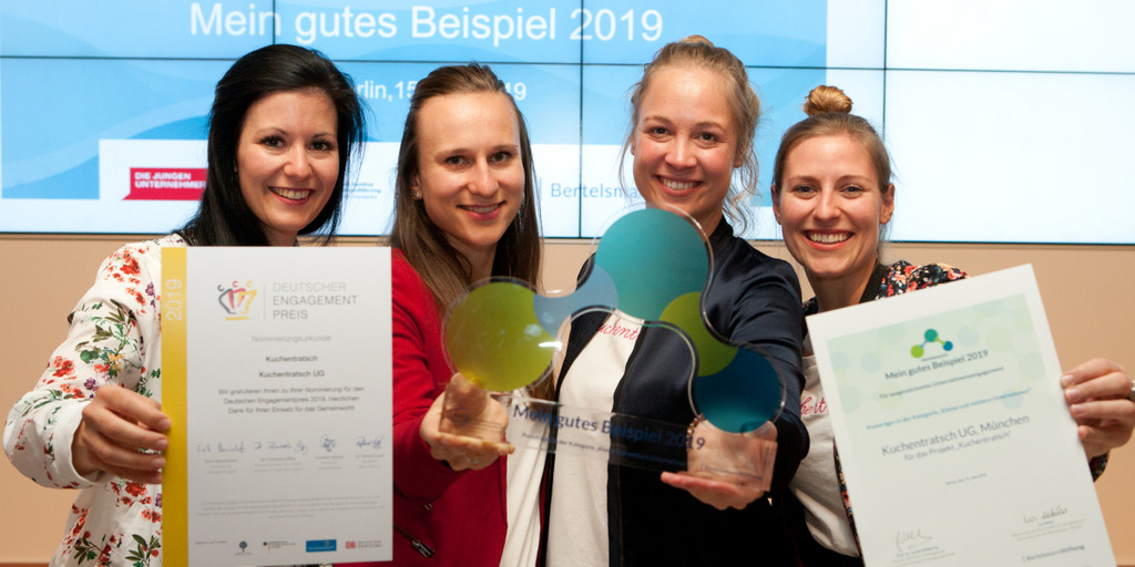 Vier Mitarbeiterinnen von "Kuchentratsch", einem der Gewinner von "Mein gutes Beispiel" 2019, halten bei der Preisverleihung im Mai 2019 in Berlin die Trophäe und ihre Gewinnerurkunden in die Kamera und lächeln.