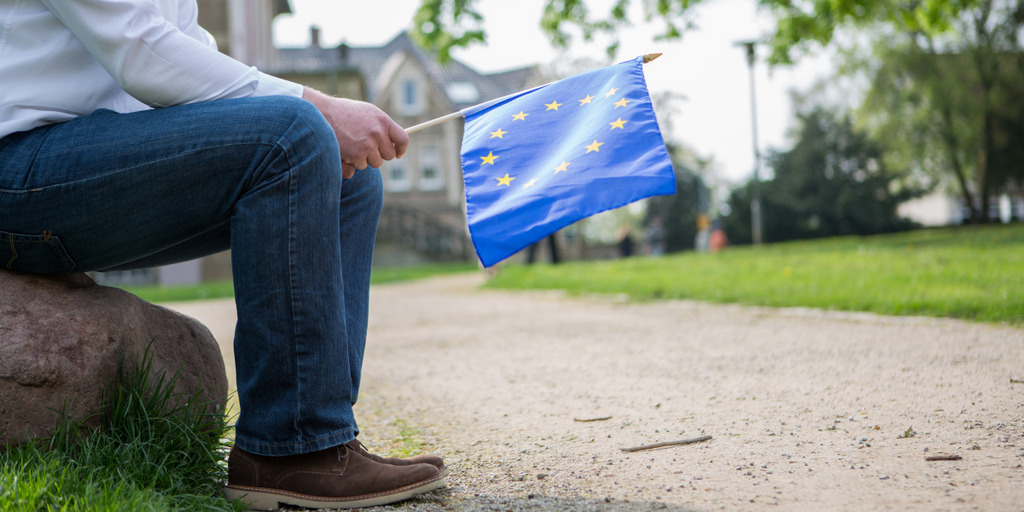 Ein Mann sitzt auf einem Stein und hält ein EU-Fähnchen in der Hand.