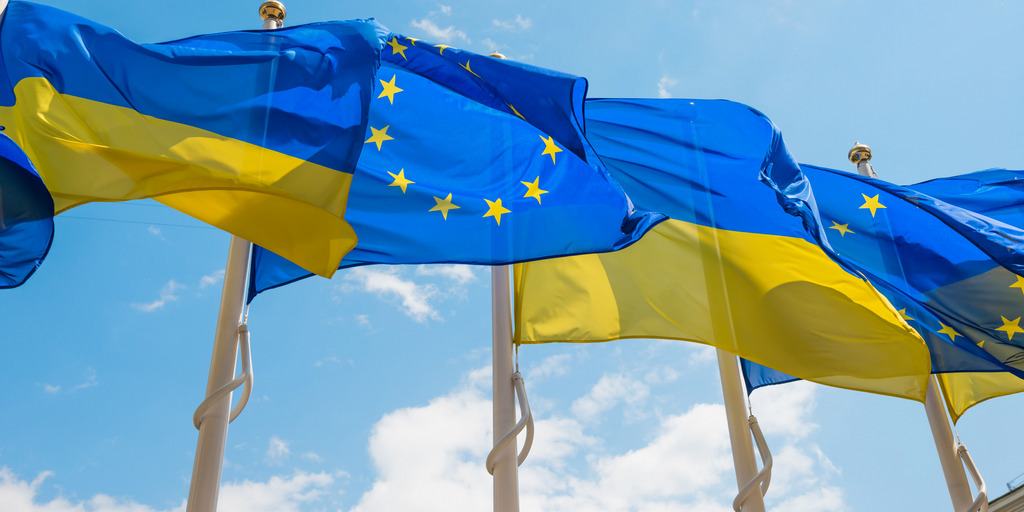Flags of Ukraine and the EU are flying on flagpoles next to each other.