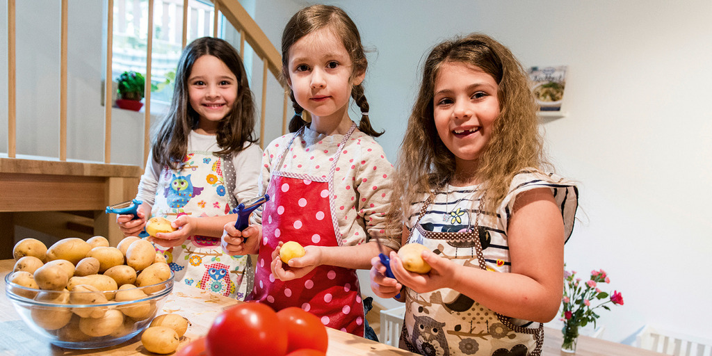 Drei junge Mädchen schälen lachend Obst in einer KiTa
