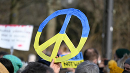 Bei einer Demonstration gegen den Krieg in der Ukraine am Brandenburger Tor in Berlin hält eine Person ein Friedens-Symbol in den Farben der ukrainischen Flagge, Blau und Gelb, in die Höhe.