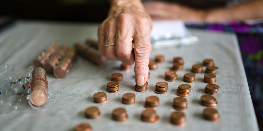 Ansicht einer Hand einer Seniorin, die auf einem Tisch liegende Cent-Stücke sortiert.