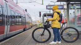 Ein Mann in Winterkleidung steht am Bahnhof und will mit seinem Fahrrad in den Zug einsteigen.