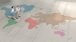 Ein Mann und eine Frau betrachten eine große auf den Boden gemalte Weltkarte. Das Bild steht symbolisch für die neue Arbeitswelt.