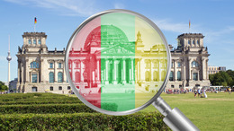Lupe mit den Koalitionsfarben Rot, Grün und Gelb auf das Reichstagsgebäude gerichtet