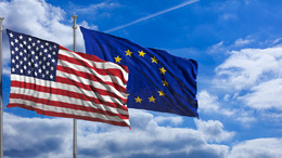 US-amerikanische und Europäische Union wehende Fahnen vor blauem Himmelhintergrund