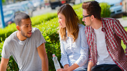 Three young people sit on a park bench and discuss.