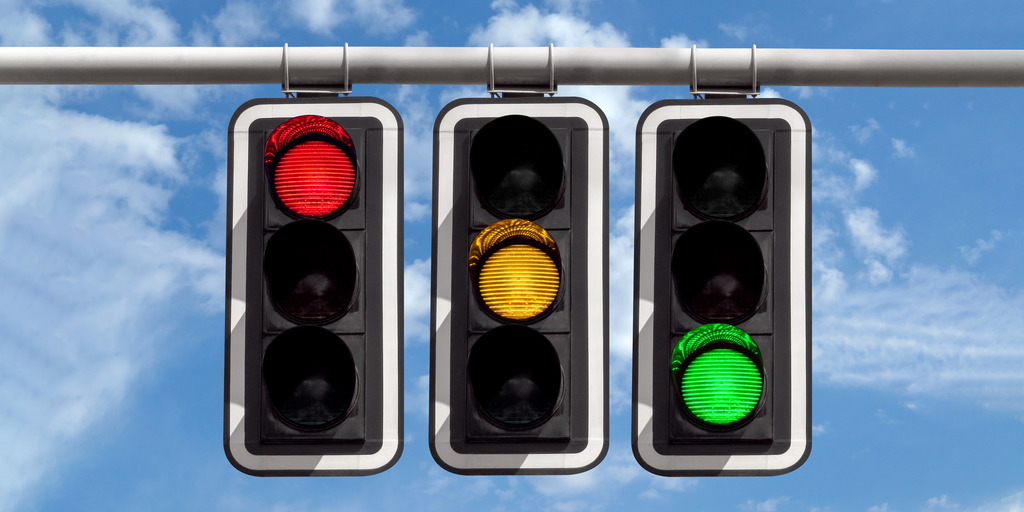 Drei Ampeln hängen nebeneinander über einer Straße. Die linke Ampel zeigt ein rotes Licht, die mittlere Ampel ein gelbes Licht, die rechte Ampel ein grünes Licht. Die Farben stehen symbolisch für SPD, FDP und Grüne.
