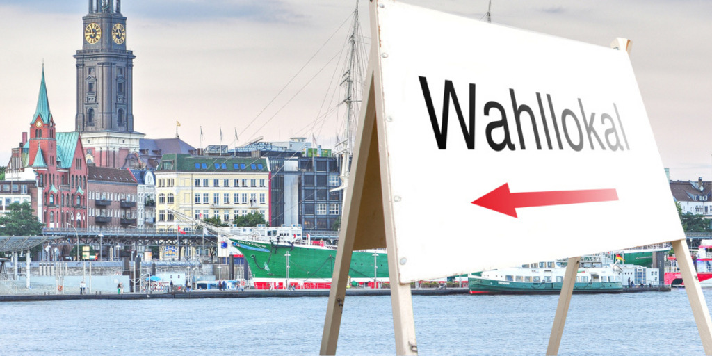 Ein Schild weist vor dem Hintergrund der Elbe, der Landungsbrücken und der Kirche St. Michaelis in Hamburg auf ein Wahllokal hin.