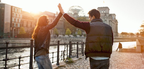 Zwei junge Menschen klatschen in die Hände ein während in an der Spree in Berlin stehen.