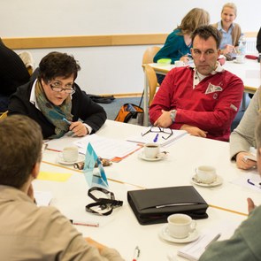 Lehrer sitzen in Gruppen an Tischen und diskutieren