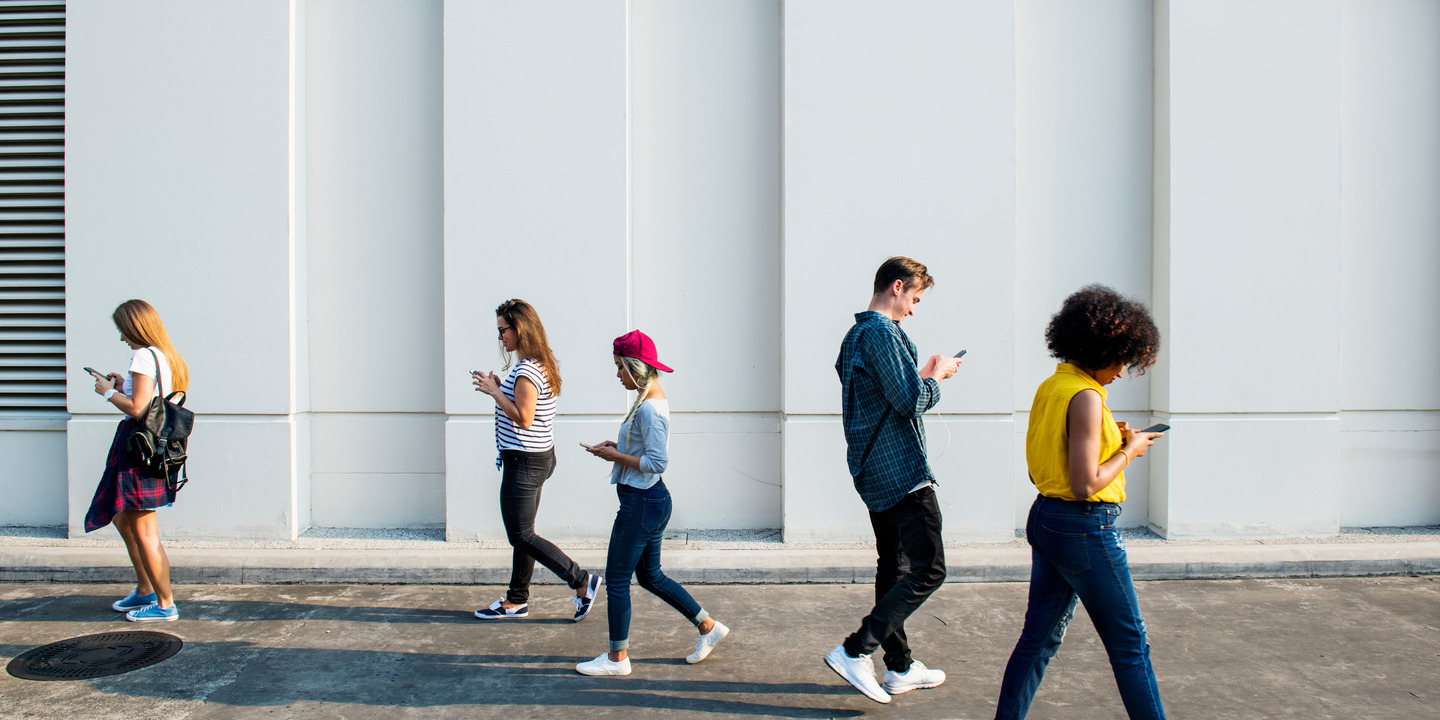 Eine Gruppe junger Menschen, die in entgegengesetzte Richtungen laufen und auf ihr Handy schauen.