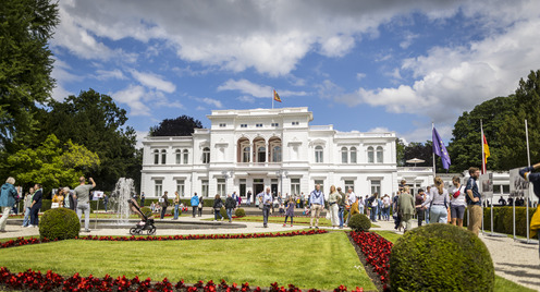 Außenansicht der Villa Hammerschmidt in Bonn an einem Tag der offenen Tür im Jahr 2024. Es sind zahlreiche Besucher:innen zu sehen, die den Park vor der Villa Hammerschmidt erkunden.