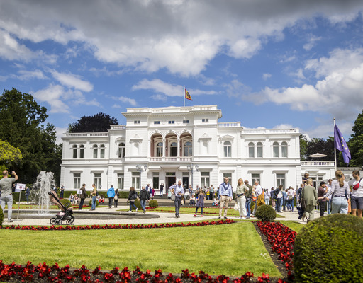Außenansicht der Villa Hammerschmidt in Bonn an einem Tag der offenen Tür im Jahr 2024. Es sind zahlreiche Besucher:innen zu sehen, die den Park vor der Villa Hammerschmidt erkunden.