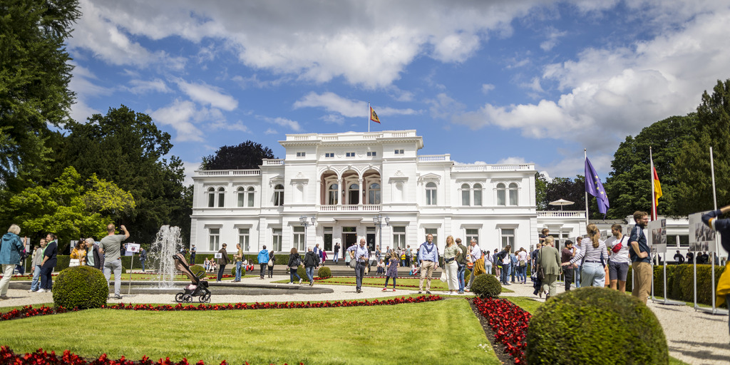 Außenansicht der Villa Hammerschmidt in Bonn an einem Tag der offenen Tür im Jahr 2024. Es sind zahlreiche Besucher:innen zu sehen, die den Park vor der Villa Hammerschmidt erkunden.