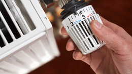 Hand turning a thermostat on a radiator