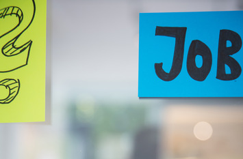 Glaswand mit bunten Post-its zu sehen. Auf einem Post-it steht Job