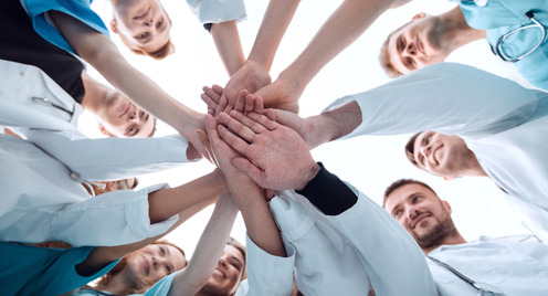 Medizinische Personal steht im Kreis und alle stapeln ihre Hände in der Mitte übereinander