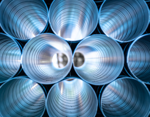 Mehrere Metallrohre liegen aufeinander gestapelt. Der Fotograf hat sie so von vorne aufgenommen, dass man der Länge nach durch die Rohre blicken kann.