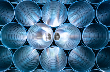 Die Aufnahme zeigt eine frontale Nahansicht mehrerer gestapelter, silberfarbener Metallrohre. Der Blick geht direkt in die kreisf&ouml;rmigen &Ouml;ffnungen, deren k&uuml;hle, bl&auml;uliche Lichtreflexionen die geriffelte Innenstruktur betonen.