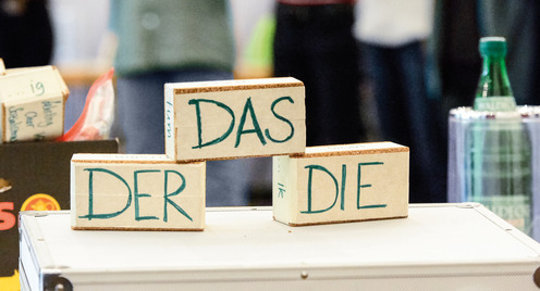 Gruppe von Lehrkräften steht hinter einem Koffer auf dem Klötzchen mit "Das", "Der", "Die" steht