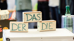 Gruppe von Lehrkräften steht hinter einem Koffer auf dem Klötzchen mit "Das", "Der", "Die" steht