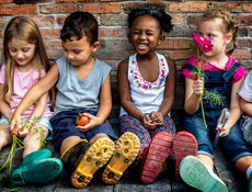 Vier Kinder sitzen auf dem Boden und halten Tomaten oder Blümchen in den Händen.