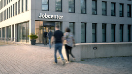 Außenaufnahme eines Jobcenters, in das mehrere Personen gehen.