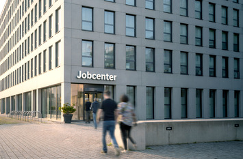 Gro&szlig;es Geb&auml;ude mit dem Titel Jobcenter. Personen im Vordergrund
