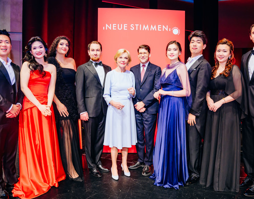 -	Liz Mohn, Präsidentin des Wettbewerbs und Vorsitzende des Vorstands der Liz Mohn Stiftung, zusammen mit Alexander Neef, Vorsitzender der Jury der NEUEN STIMMEN, und den Finalist:innen des Wettbewerbs 2026.
