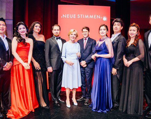 -	Liz Mohn, Präsidentin des Wettbewerbs und Vorsitzende des Vorstands der Liz Mohn Stiftung, zusammen mit Alexander Neef, Vorsitzender der Jury der NEUEN STIMMEN, und den Finalist:innen des Wettbewerbs 2026.