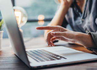 Zwei Personen blicken auf einen Laptop-Bildschirm. Eine der beiden Personen zeigt mit dem Finger auf den Bildschirm.
