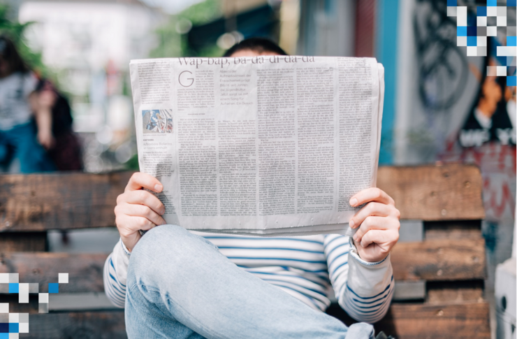 Person sitzt auf einer Bank im Park und schaut sich eine Zeitung an, die seinen Oberk&ouml;rper sowie Gesicht verdeckt.