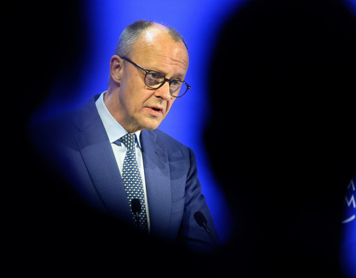 Der deutsche Bundeskanzler Friedrich Merz hält vor dem Weltwirtschaftsforum 2026 in Davos eine Rede. Er ist am Rednerpult zu sehen, zwischen den Hinterköpfen zweier Zuhörender, die nur als Schatten zu erkennen sind.