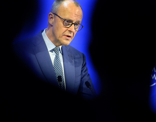 Der deutsche Bundeskanzler Friedrich Merz hält vor dem Weltwirtschaftsforum 2026 in Davos eine Rede. Er ist am Rednerpult zu sehen, zwischen den Hinterköpfen zweier Zuhörender, die nur als Schatten zu erkennen sind.