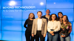 Sechs Personen stehen vor einer blauen Wand mit der Aufschrift 'BEYOND TECHNOLOGY: AI & Data for the Common Good 17. September 2026' und lächeln in die Kamera