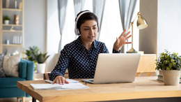 Frau mit Kopfhörern arbeitet im Homeoffice am Laptop