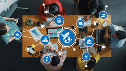 Eine Gruppe von Menschen sitzt an einem Holztisch in einer Besprechung, darüber liegt eine digitale Grafik vernetzter Icons zu den Themen Nachhaltigkeit, Umweltschutz und globale Vernetzung.