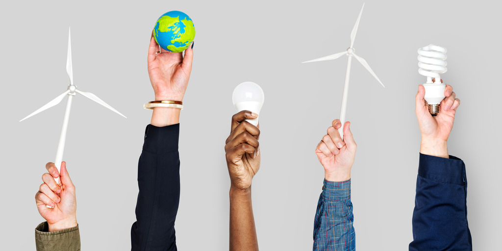 Verschiedene Personen strecken ihre Hände in die Höhe und halten jeweils einen Gegenstand in der Hand, der für Klimaschutz beziehungsweise die Energiewende steht: Windräder, eine Miniatur-Erdkugel, eine LED-Leuchte sowie eine Energiesparlampe.