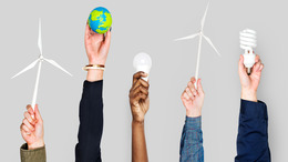 Verschiedene Personen strecken ihre Hände in die Höhe und halten jeweils einen Gegenstand in der Hand, der für Klimaschutz beziehungsweise die Energiewende steht: Windräder, eine Miniatur-Erdkugel, eine LED-Leuchte sowie eine Energiesparlampe.