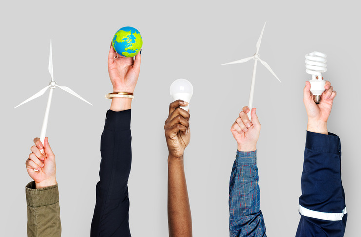 Verschiedene Personen strecken ihre H&auml;nde in die H&ouml;he und halten jeweils einen Gegenstand in der Hand, der f&uuml;r Klimaschutz beziehungsweise die Energiewende steht: Windr&auml;der, eine Miniatur-Erdkugel, eine LED-Leuchte sowie eine Energiesparlampe.
