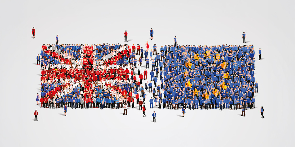 The image shows a high-angle, birds-eye view of a large crowd of stylized human figures arranged against a neutral, light gray background. The people are positioned to form two distinct blocks that visually represent national flags.