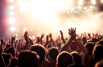 Publikum mit erhobenen H&auml;nden auf einem Musikfestival, Lichtstrahlen fallen von oben auf die B&uuml;hne